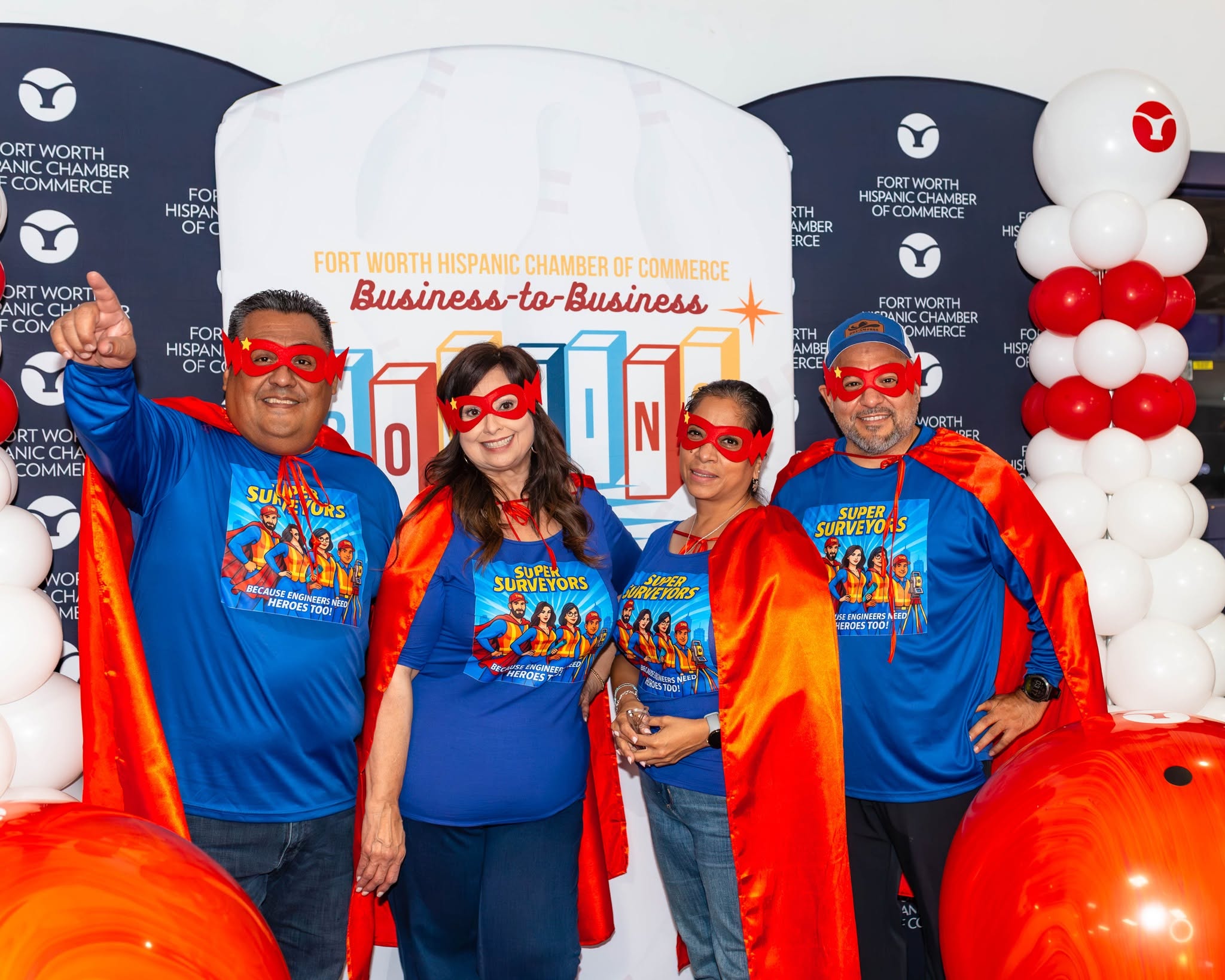 Four people wearing superhero shirts and red capes
