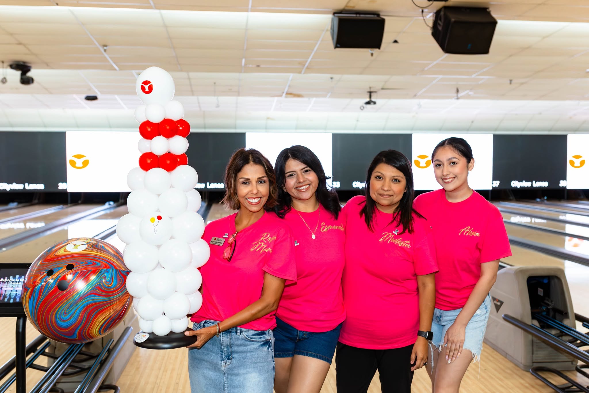 Four women in pink shirts at bowling alley